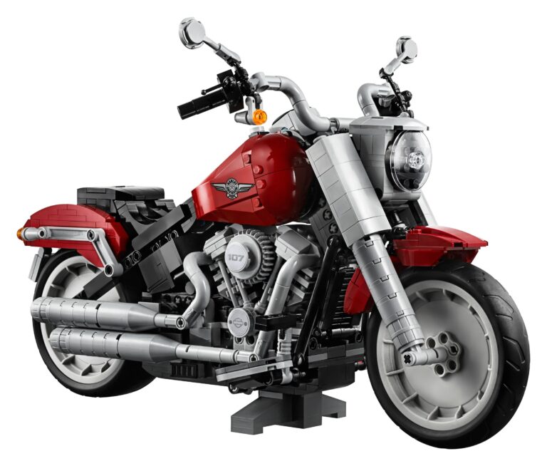 Il LEGO 10269 Harley-Davidson Fat Boy visto di tre quarti anteriore su sfondo bianco, con il serbatoio a goccia rosso scuro, le forcelle anteriori grigie, il faro rotondo, le ruote a disco pieno e un supporto grigio scuro sotto il motore