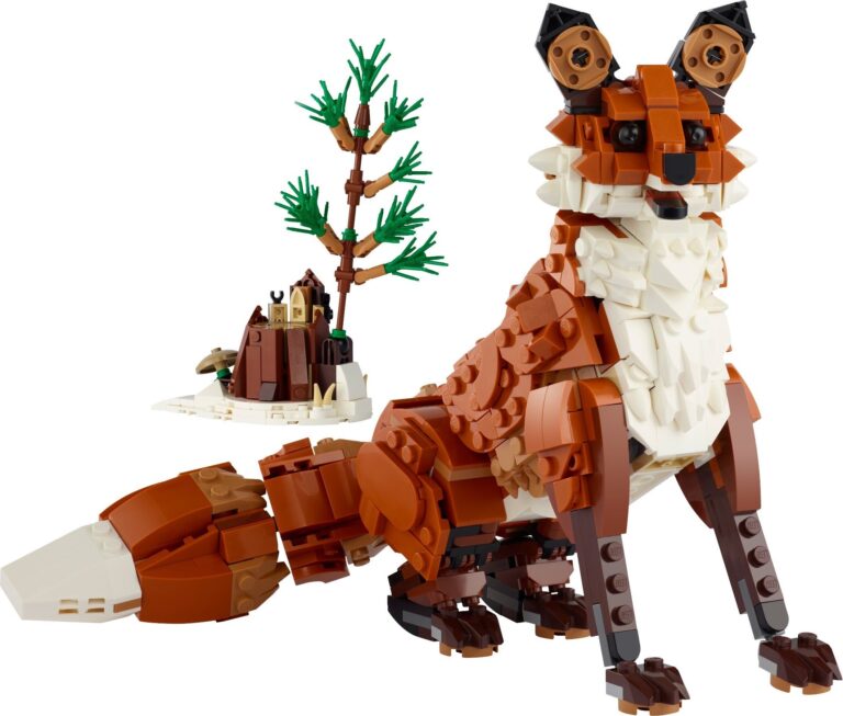 LEGO rudoji lapė iš rinkinio 31154 sėdi ant balto fono, oranžiniu kūnu, balta krūtine ir uodegos galiuku, juodomis ausimis ir nosimi, šalia apsnigto kelmo su maža iš kaladėlių pastatyta egle ir grybu